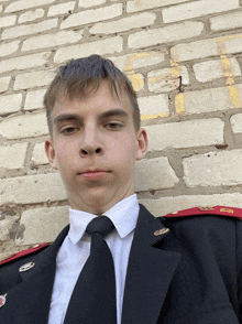 a young man in a suit and tie is standing in front of a brick wall