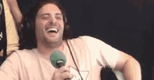a man wearing headphones is laughing and holding a green microphone .