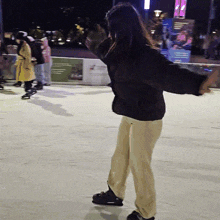 a woman in a black jacket is standing on a ice rink with her arms outstretched