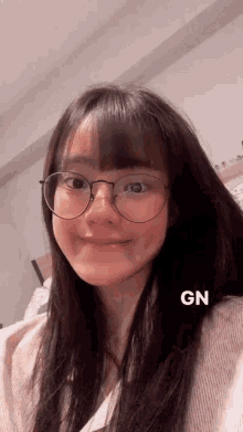 a girl wearing glasses and a white shirt has the word gn on the bottom right