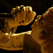 a close up of a person singing into a microphone with rings on their fingers