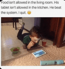 a child is laying on the floor eating food and looking at a tablet ..