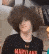 a young man with a big curly hair is wearing a maryland shirt .