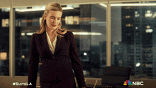 a woman in a suit is standing in front of a window with nbc written on the bottom