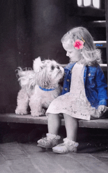 a little girl with a flower in her hair is sitting next to a dog