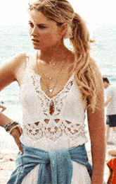 a woman wearing a white lace top and a denim jacket is standing on a beach