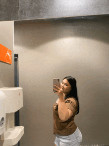 a woman taking a selfie in a bathroom next to a hand dryer
