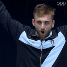 a man wearing a blue and white ea7 jacket stands with his arms in the air