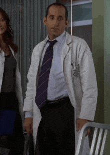 a man in a white coat and purple tie stands next to a woman