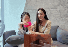 two women are sitting on a couch and one of them is holding a pink cup that says coca cola
