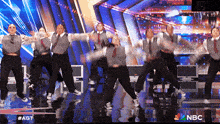 a group of people dancing on a stage with a nbc logo in the background