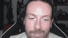 a man with long hair and a beard is sitting in a chair looking at the camera .
