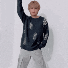 a young man wearing a black sweater and grey pants is standing in front of a white wall