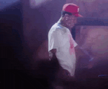 a man wearing a red hat and a white shirt is standing on a stage in a dark room .