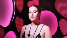 a woman in a black bra is standing in front of pink hearts on a stage .