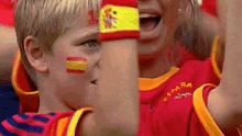 a boy with spanish flags painted on his face is wearing a spain shirt