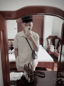 a young man taking a selfie in front of a mirror with a purse that says idola 2 on it