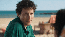 a young man with curly hair is sitting on the beach