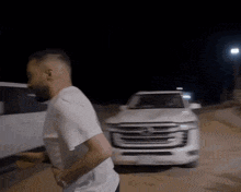 a man in a white shirt is running in front of a white car at night