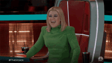 a woman in a green dress laughs while sitting in front of a nbc logo