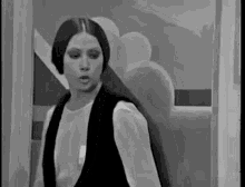a black and white photo of a woman with long hair standing in front of a window .