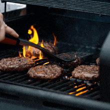 a person is cooking hamburgers on a grill with flames