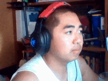 a man wearing headphones and a red hat is sitting in front of a bookshelf .