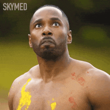 a shirtless man with yellow paint on his chest and the word skymed on the bottom