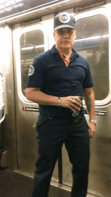 a man in a blue shirt and hat stands in front of a door that says do not hold doors