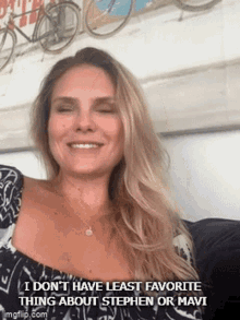 a woman is sitting on a couch and smiling while wearing a necklace and a blue top .
