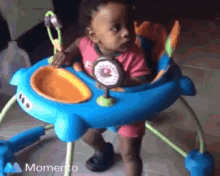 a baby in a blue and orange walker with the word momento on the bottom right