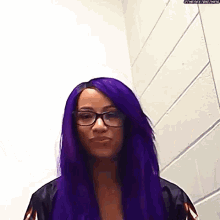 a woman with purple hair and glasses is standing next to a wall .
