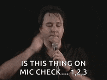 a man is holding a microphone and saying is this thing on mic check
