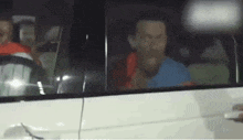 a man in a blue shirt is sitting in a white car .