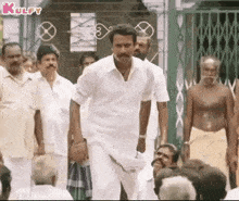 a man in a white shirt and a mustache is standing in front of a crowd of people .