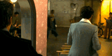 a man in a suit stands in front of a mirror looking at his reflection