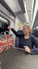 a woman is sitting on a train with a bag that says m & s on it .