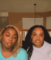 two women are sitting next to each other in a living room and looking at the camera