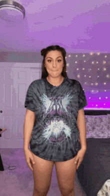 a woman wearing a tie dye t-shirt is standing in front of a purple wall