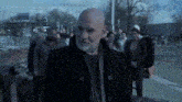 a bald man with a beard is walking down the street with a group of people .