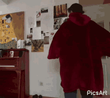 a person wearing a red hoodie is standing in front of a piano in a room with picsart written on the bottom