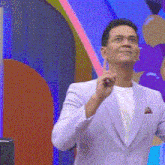 a man in a white suit and white shirt is standing in front of a colorful wall .