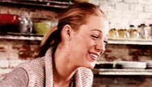 a woman in a sweater is smiling while sitting at a table in a kitchen .