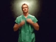 a man in a green scrub is standing in a dark room .