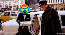 a man in a tuxedo is holding a box of pizza next to a limo