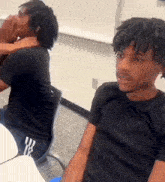 two young men are sitting at a table in a classroom and one of them is covering his mouth with his hand .
