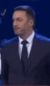 a man in a suit and tie is standing in front of a microphone .