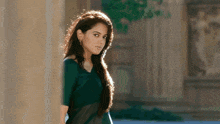 a woman in a green top is standing next to a pillar