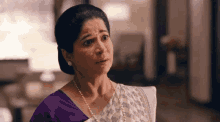 a woman wearing a purple blouse and pearls is making a funny face