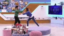 a man and a woman are fighting in a living room with a tv in the background .